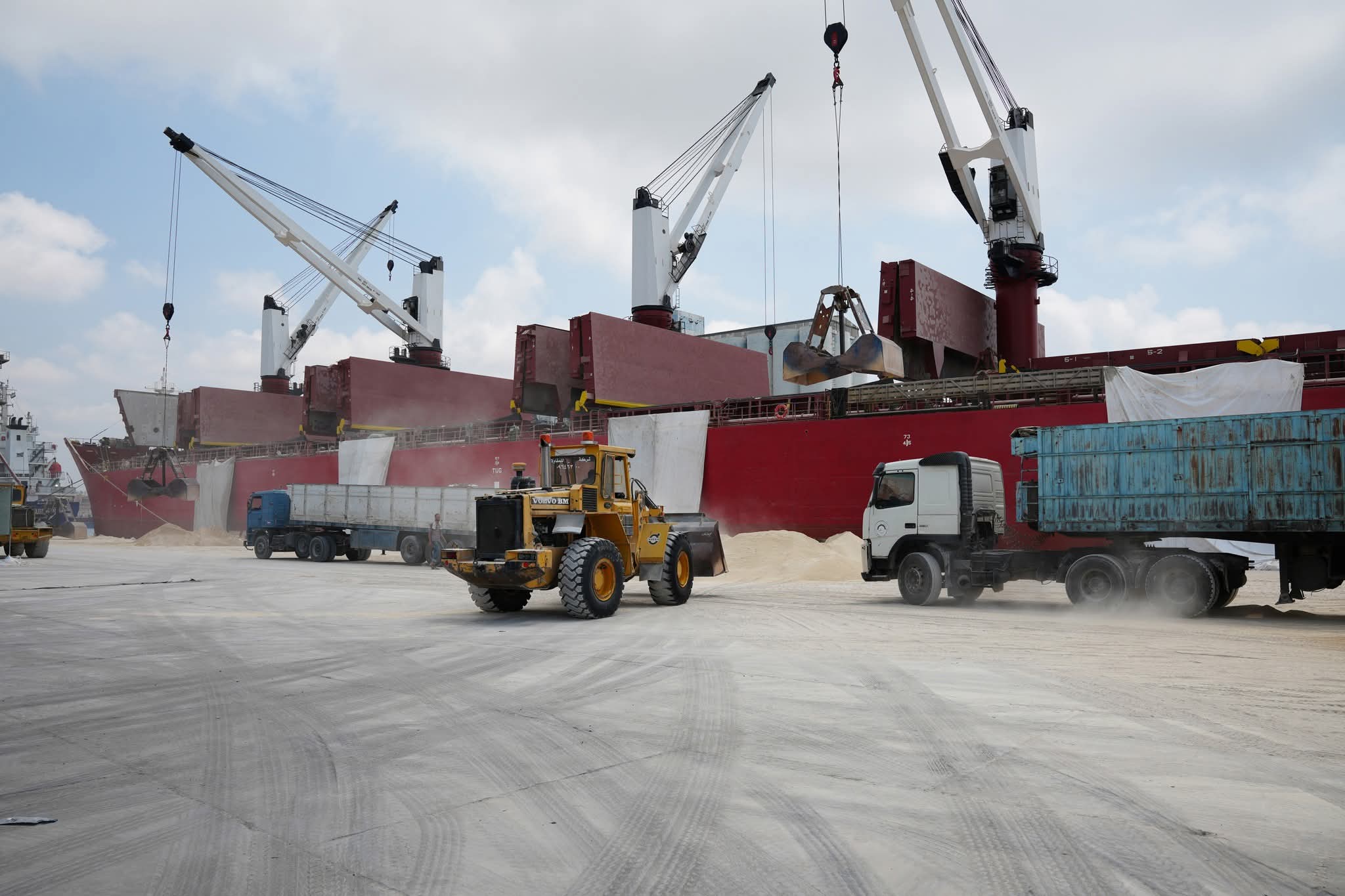 Geared bulk carrier discharging alongside, trucks and wheel loader working the berth apron